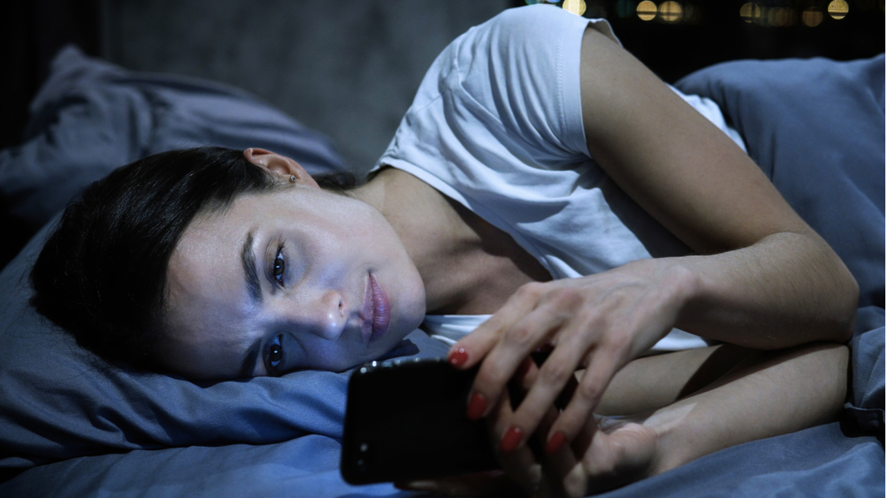 mujer echada en cama con celular