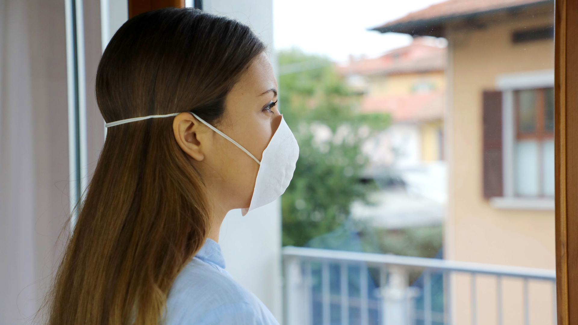 mujer con mascarilla viendo por su ventana