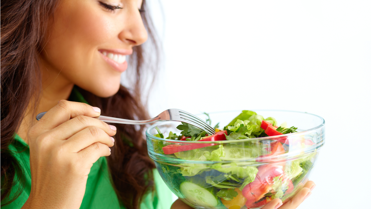 mujer sonrie mientras come ensalada